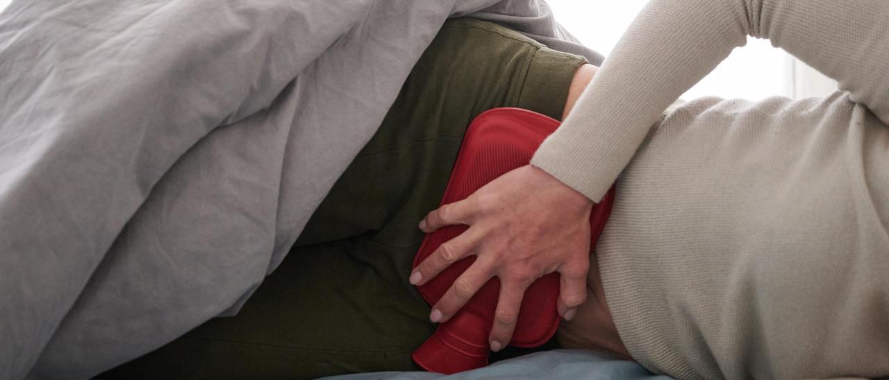 Eine Frau hält sich eine Wärmflasche an den Unterbauch, während sie im Bett liegt (gestellte Szene). Viele Betroffene der Unterleibserkrankung Endometriose leiden unter starken Symptomen und damit verbundenen Einschränkungen im Alltag.