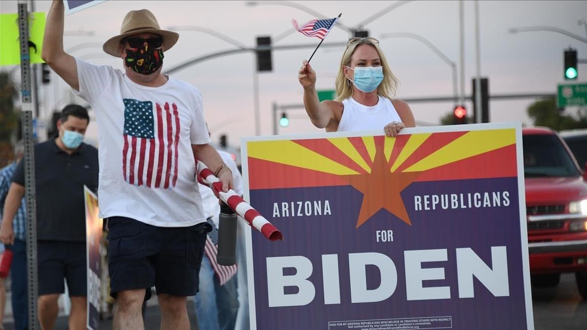 Miembros del grupo Republicanos de Arizona que creen en tratar a los otros con respeto ondean banderas y un cartel en apoyo a Biden.