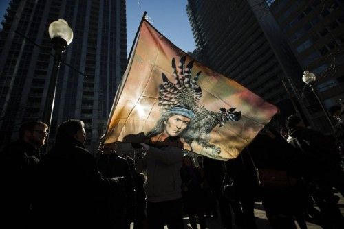 First Nations protesters are silhouetted against a flag as the take in a  "Idle No More" demonstration in Toronto