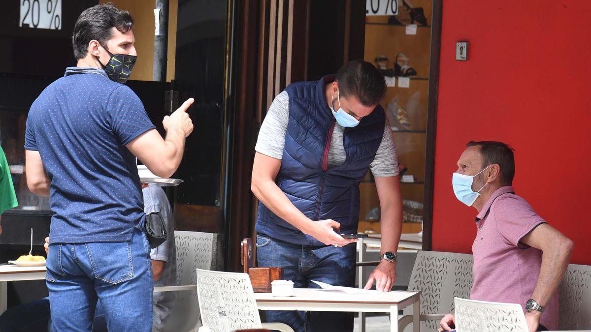 Tres hombres con mascarilla en una terraza coruñesa.