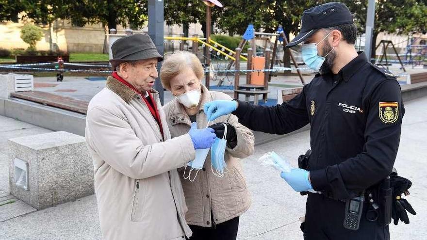 Un agente de la Policía Nacional reparte mascarillas en la plaza de Pontevedra de A Coruña.