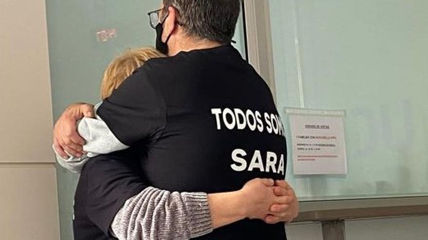 Los padres de Sara, con camisetas en su apoyo, se dan un abrazo.