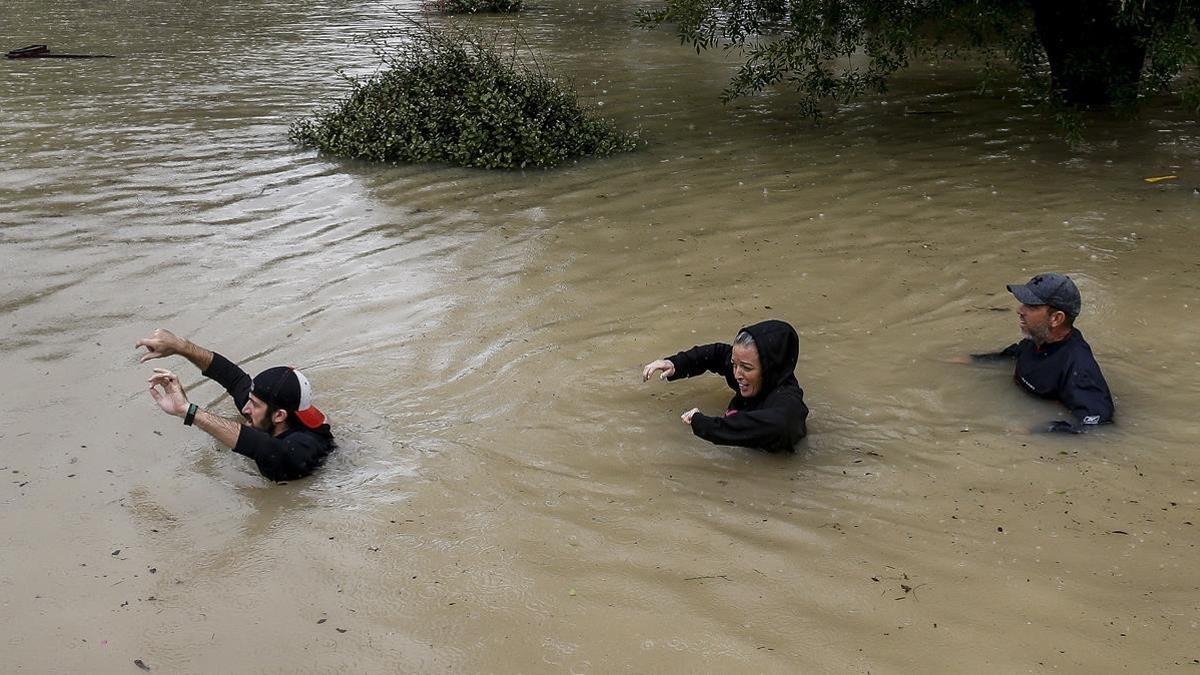 Tres personas cruzan un río de Houston cerca del embalse de Addicks, que amenaza con desbordarse.