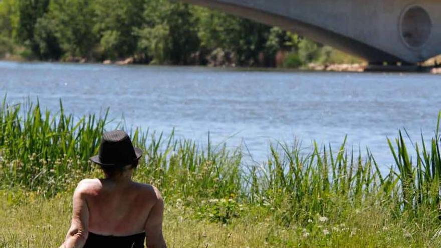 Una mujer toma el sol junto al río.