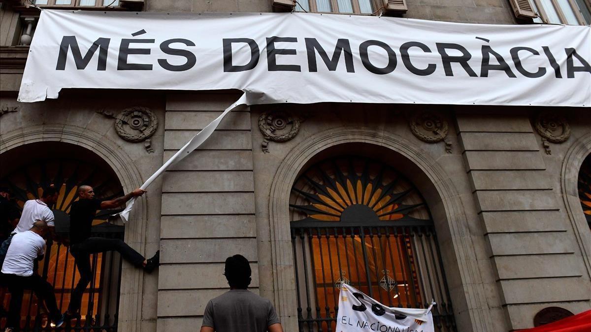 Unos manifestantes antiindependentistas intentan descolgar sin éxito la pancarta de Más Democracia del Ayuntamiento.