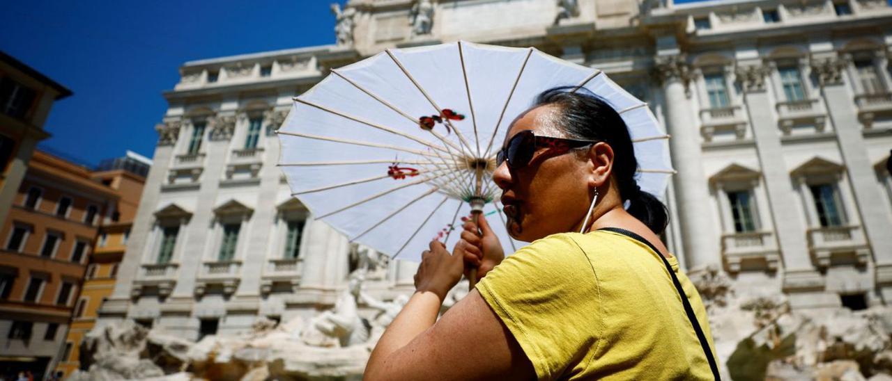 Una turista se protege bajo un parasol mientras se refresca en la Fontana di Trevi, en Roma.