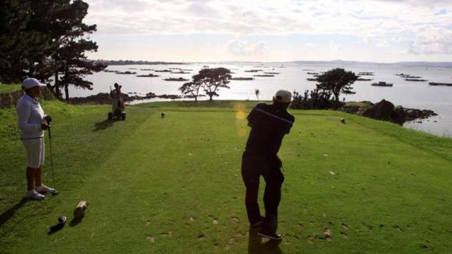 Un golfista golpea la bola en el campo de golf de A Toxa con las bateas al fondo.  // Muñiz