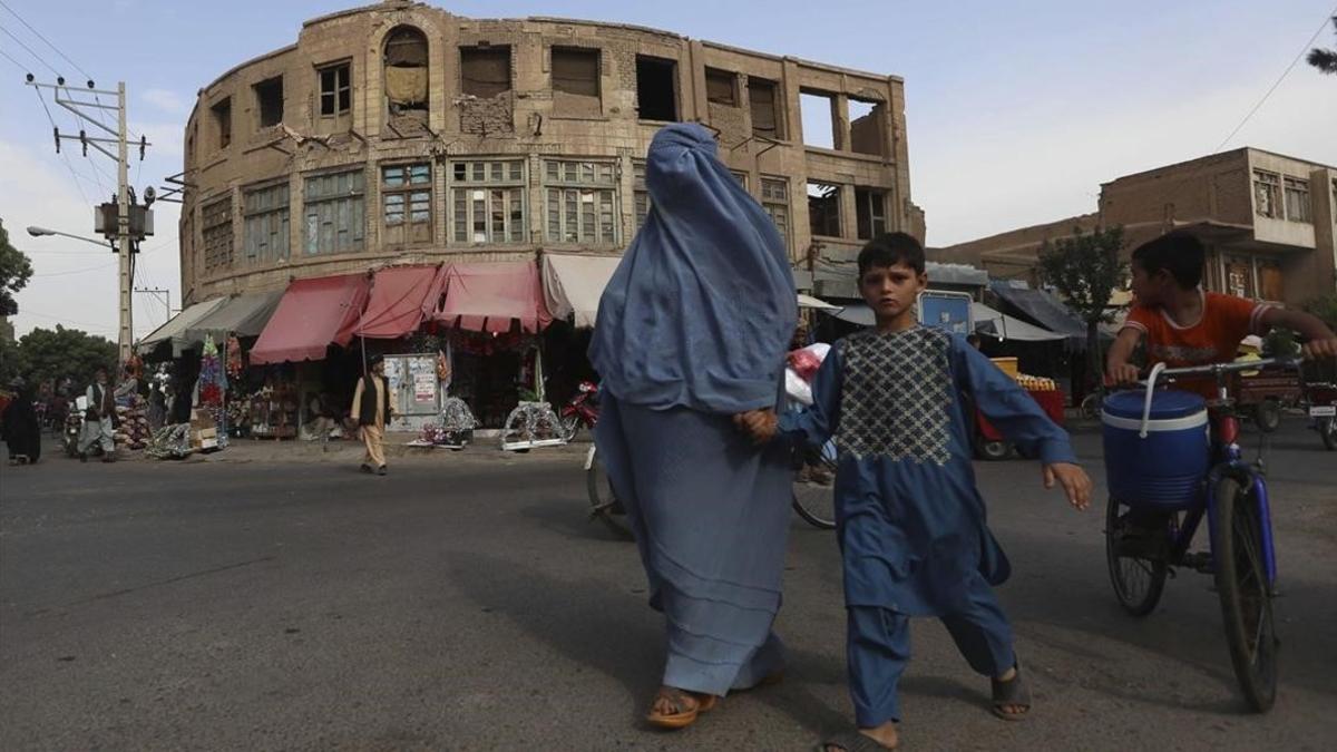 Una mujer afgana vestida con un burka agarra de la mano a su hijo al cruzar una calle en Herat, Afganistán, este jueves.