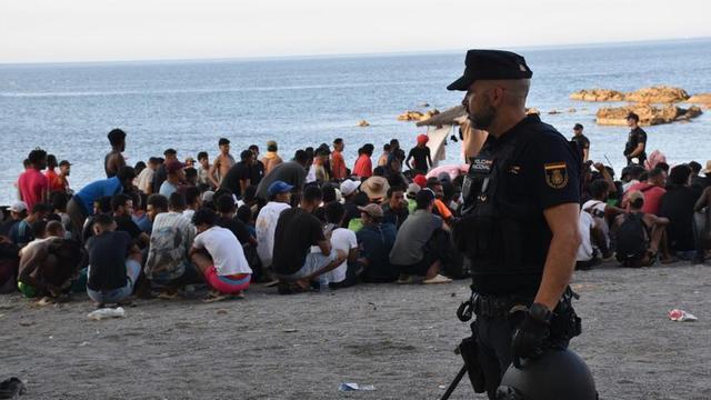Un policia nacional, davant desenes de migrants, el cap de setmana passat en una platja de Ceuta. | GABRIELA SARDÁ NÚÑEZ / EUROPA PRESS