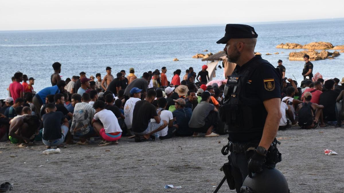 Un policia nacional, davant desenes de migrants, el cap de setmana passat en una platja de Ceuta. | GABRIELA SARDÁ NÚÑEZ / EUROPA PRESS