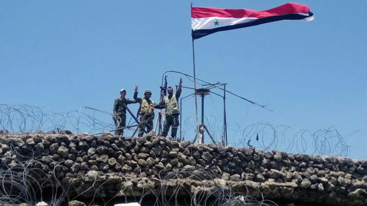 Las tropas gubernamentales muestran el signo de la victoria al lado de la bandera siria en Daraa.