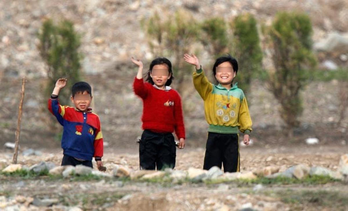 Uns nens nord-coreans de la ciutat de Chongsong saluden uns turistes que passen en vaixell per Dangdong (Xina) a l’altre costat de la frontera.