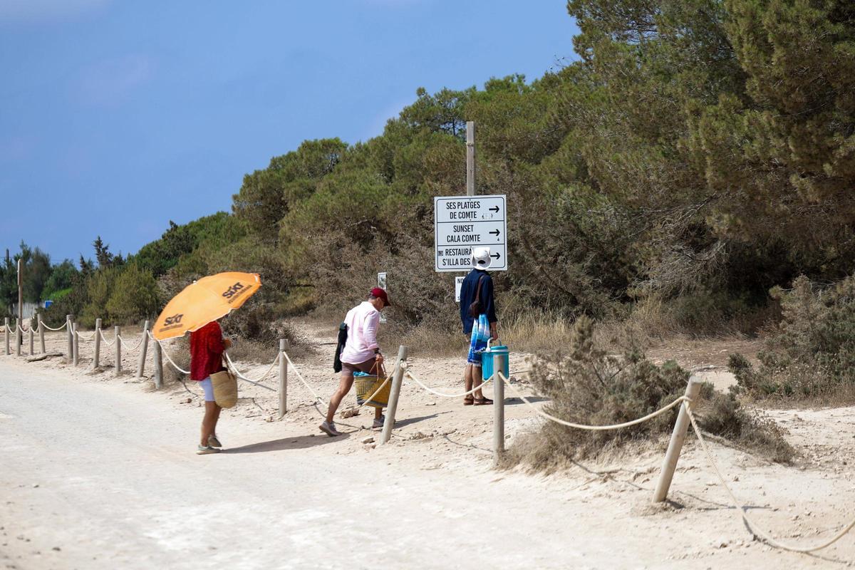 Visitantes atraviesan el parking para llegar a la playa.