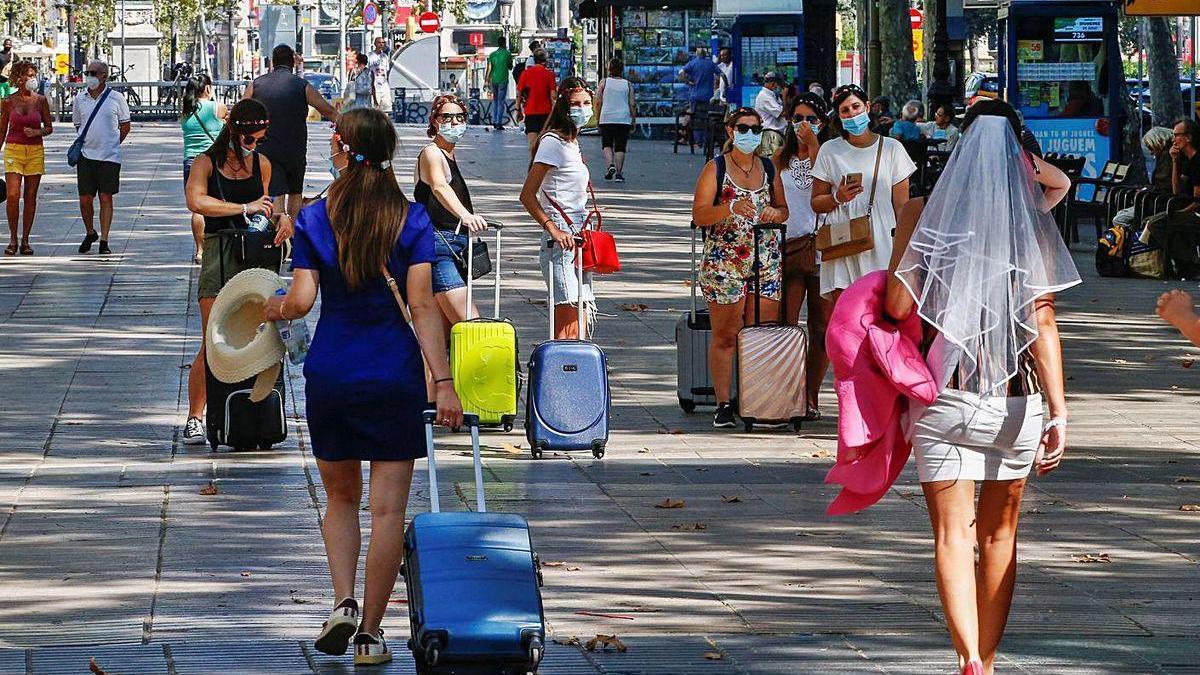 Turistas con maletas y mascarillas, ayer, en una calle de Barcelona.