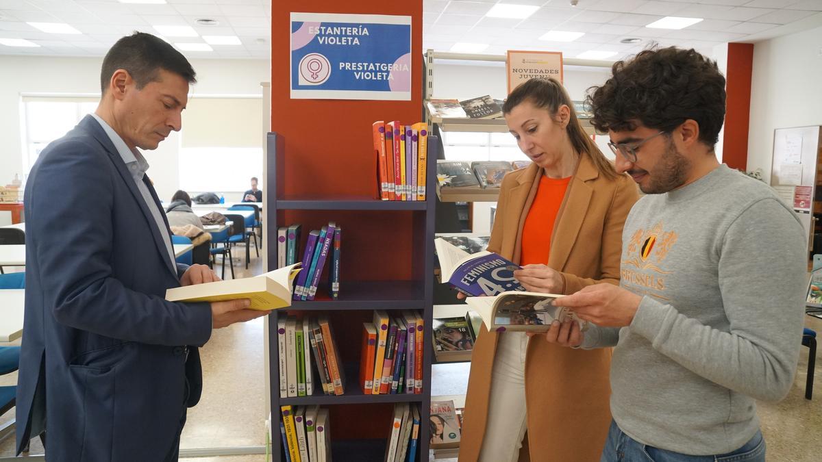 El alcalde ojea un libro de la estantería violeta de la Biblioteca de Burjassot.