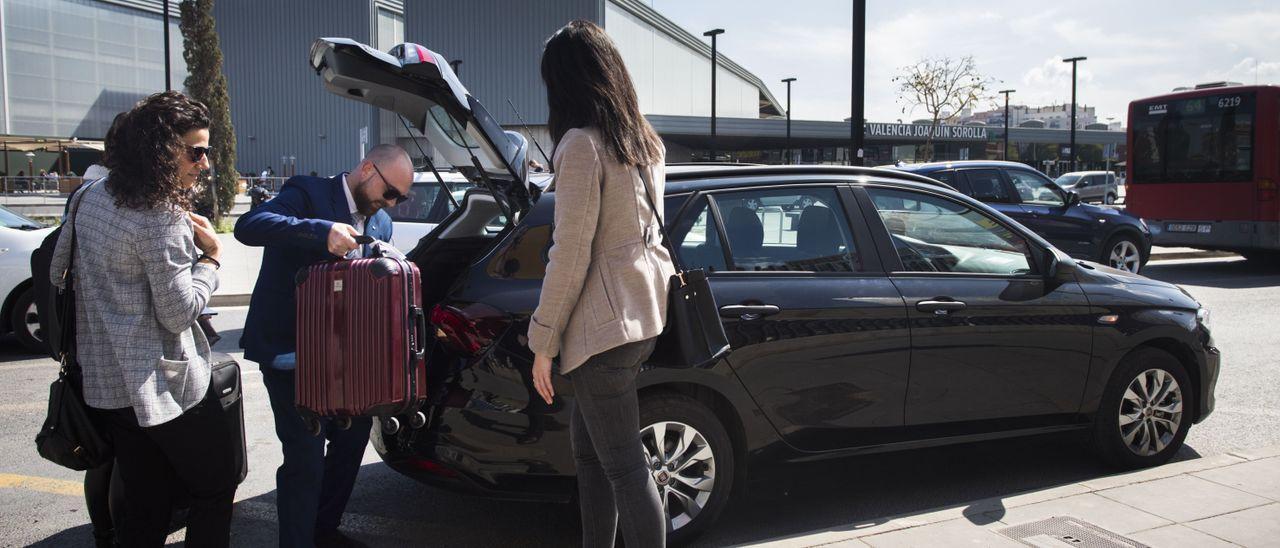 Un conductor de un servicio de VTC recoge la maleta de una clienta en la estación del AVE de València.