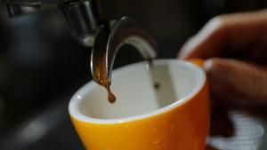 Una taza con el café saliendo de una cafetera automática.
