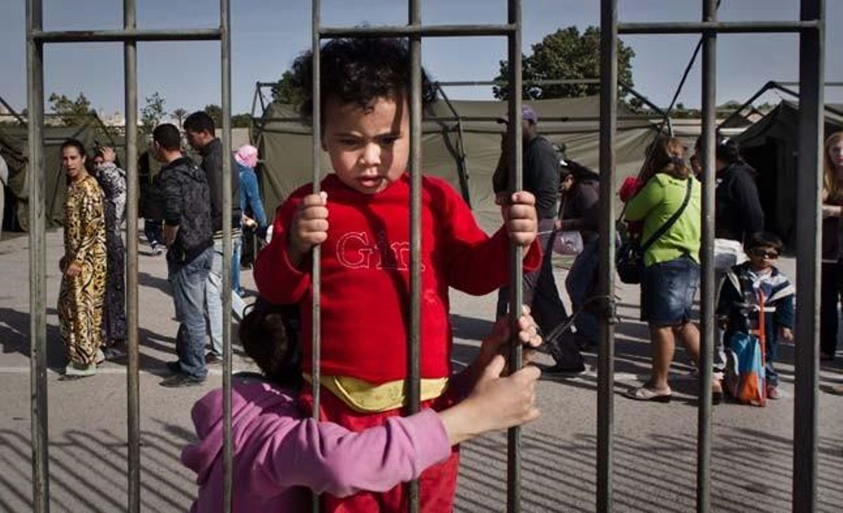 Una nena mira a través de la reixa que delimita un dels campaments instal·lats per la Unitat Militar d’Emergències a Llorca.