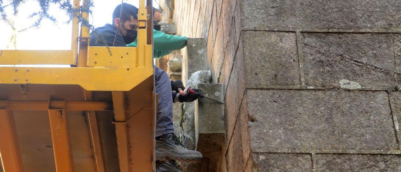 El “canteiro” y el restaurador, ayer subidos a la máquina elevadora para picar la cruz.  | // NOÉ PARGA