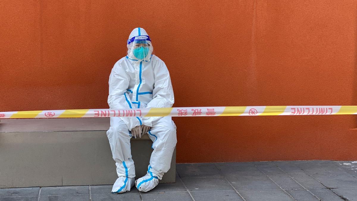 Worker in a protective suit sits near a police line outside a store, following the coronavirus disease (COVID-19) outbreak in Shanghai