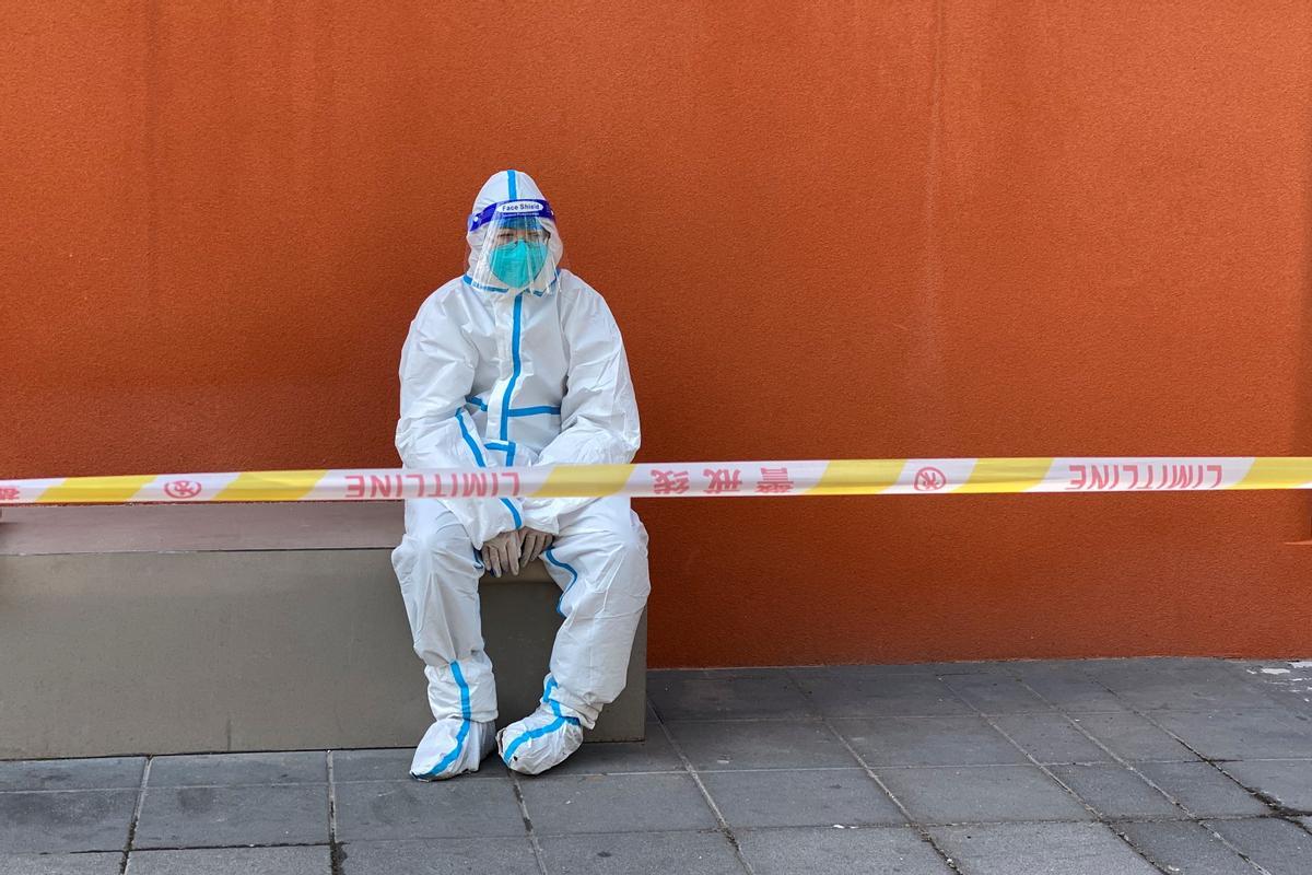 Worker in a protective suit sits near a police line outside a store, following the coronavirus disease (COVID-19) outbreak in Shanghai