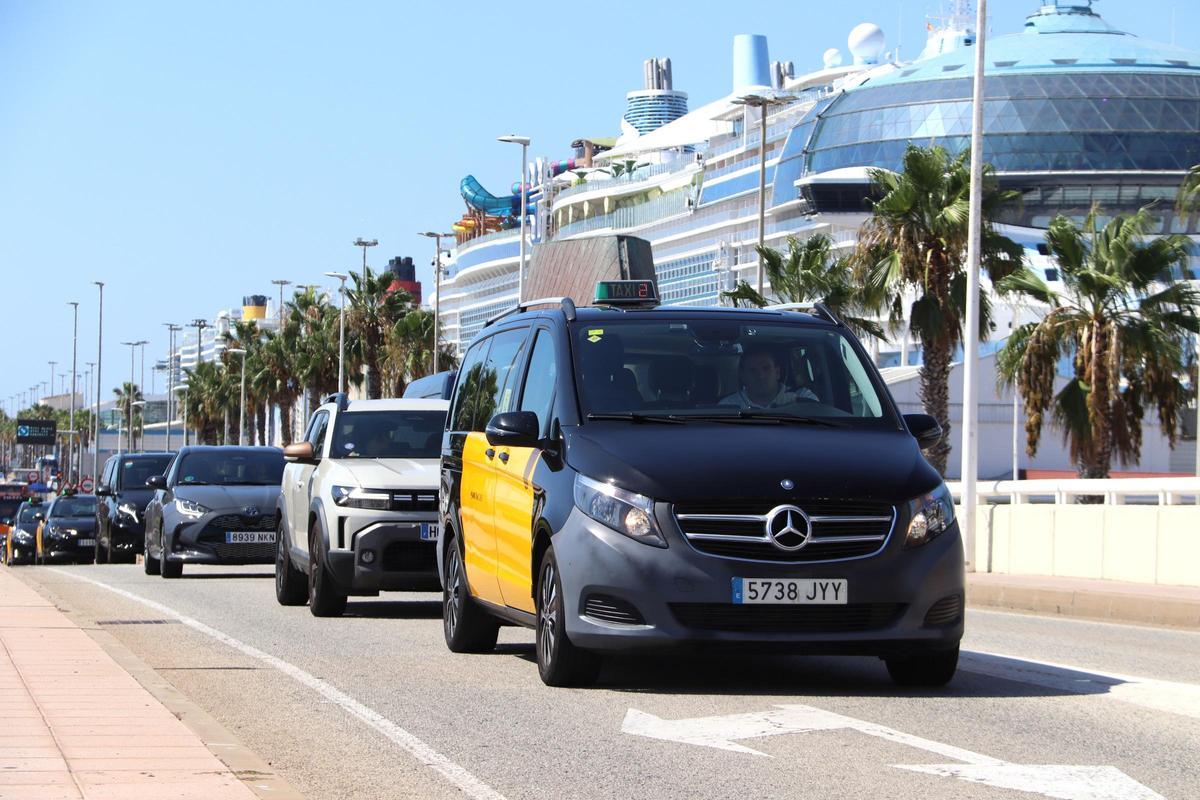 Un taxista circula, seguido de otros vehículos, en el muelle adosado del Port de Barcelona, con un crucero al fondo
