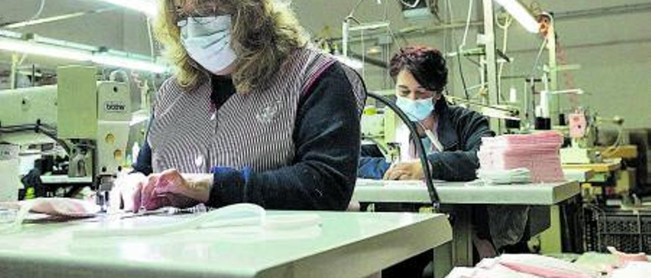 Trabajadoras de la textil Errequeerre fabricando mascarillas el 1 de abril de 2020 y, a la derecha, dos empleados en Mapubli, especializada en la producción de mamparas, el pasado mes de mayo.  GERMÁN CABALLERO
