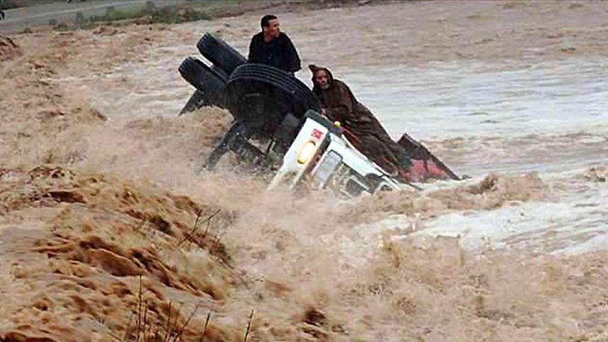 Dos conductores se agarran como pueden a un camión casi hundido y arrastrado por las aguas, en la región de Ouarzazate, este sábado.