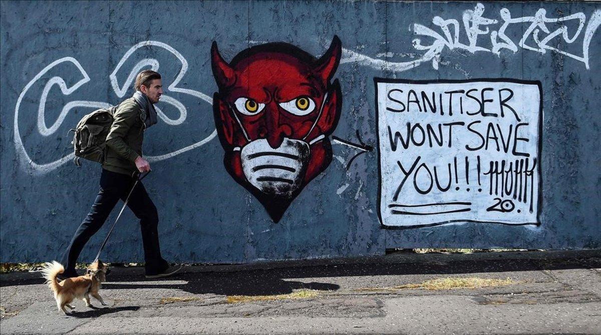 Un hombre y su perro pasean frente a un mural alusivo a la crisis del coronavirus en Glasgow, Escocia.