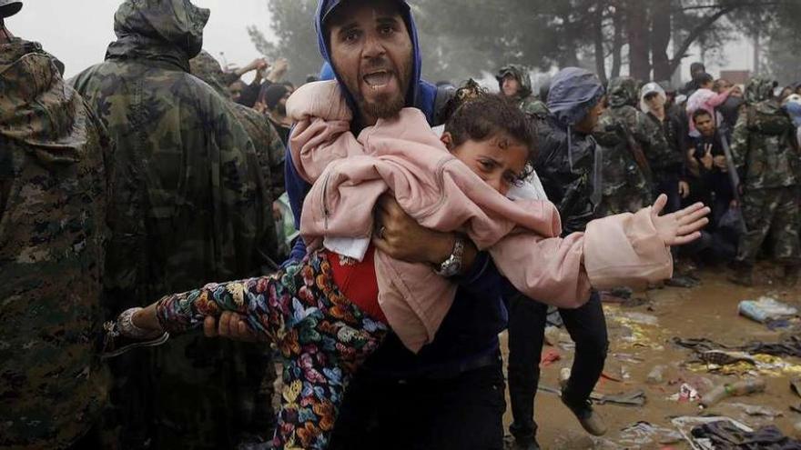 Un refugiado sirio camina entre el barro con un niño en brazos en la frontera entre Grecia y Macedonia, cerca de la localidad helena de Idomeni. // Reuters