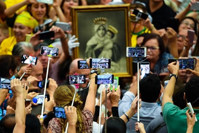 Los fieles, con palitos selfie y teléfonos móviles, toman fotos del Papa Francisco mientras llega a su audiencia general semanal en la sala Pablo VI.