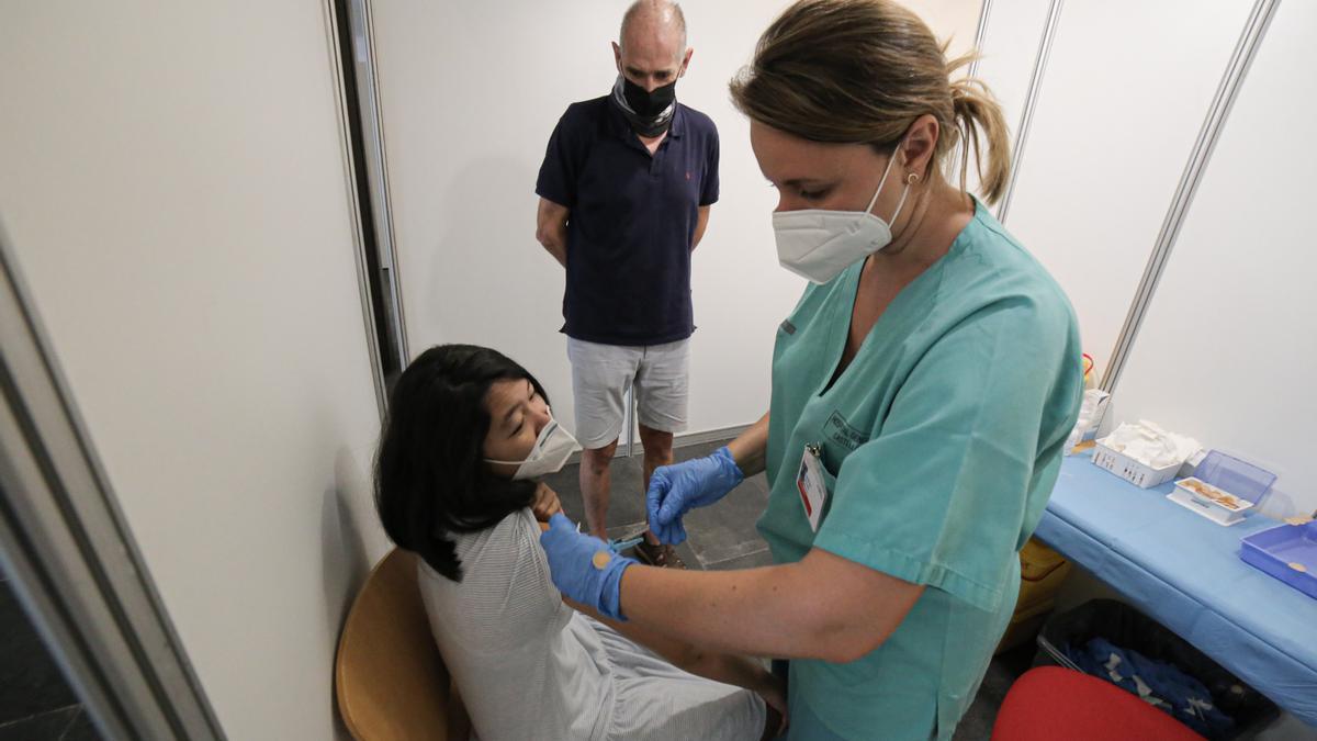 Una joven recibe la vacuna ante la mirada de su padre.