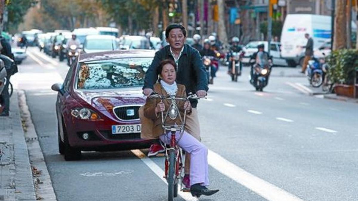 Una pareja de ciudadanos chinos circula en una bici del Bicing por la calle Consell de Cent después de sortear un coche parado en su carril, ayer.