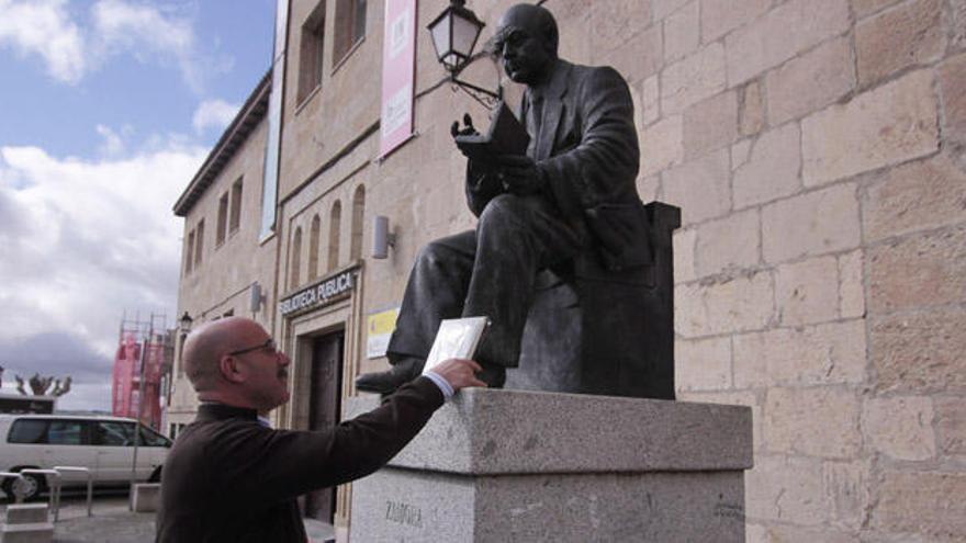 Un hombre coge un libro depositado en una estatua de Zamora