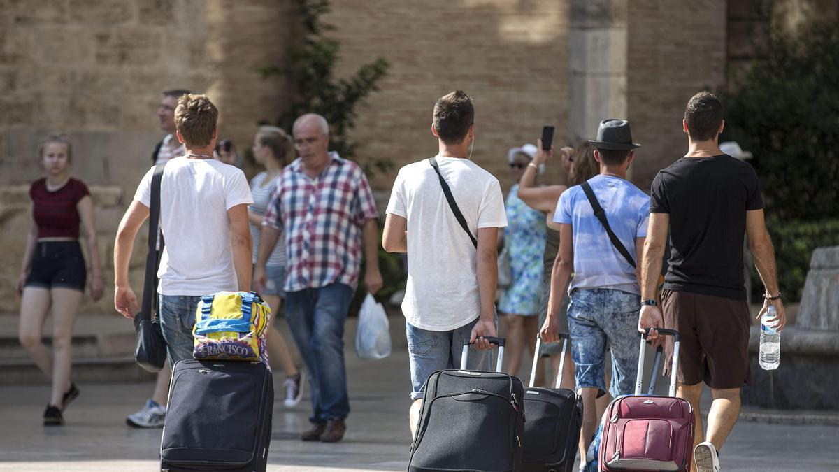 Varias personas arrastran sus maletas por la calle.