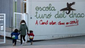 Una mujer acompaña a dos niños a la escuela Turó del Drac de Canet de Mar, en cuya entrada luce una pintada que reclama la enseñanza en catalán.