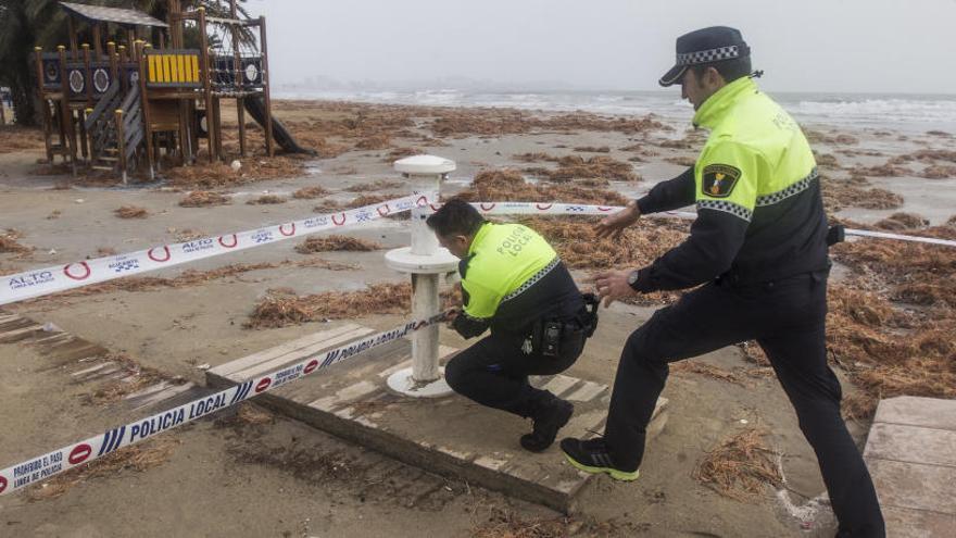 Dos policías colocan el precinto para prohibir el paso a la arena de la playa del Postiguet, ayer.