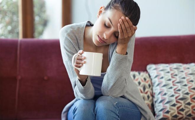 FOTO BAJADA DE 123RF EL 14 DE ENERO DEL 2021 PARA ILUSTRAR UN ARTICULO SOBRE EL  BLUE MONDAY   EL DIA MAS TRISTE DEL ANO SEGUN UN ALGORITMO MATEMATICO  CHICA TRISTE  TRISTEZA  DEPRESION  REFLEXION  shot of depressed young woman having headache while drinking coffee on sofa at home  FOTO DE 123RF