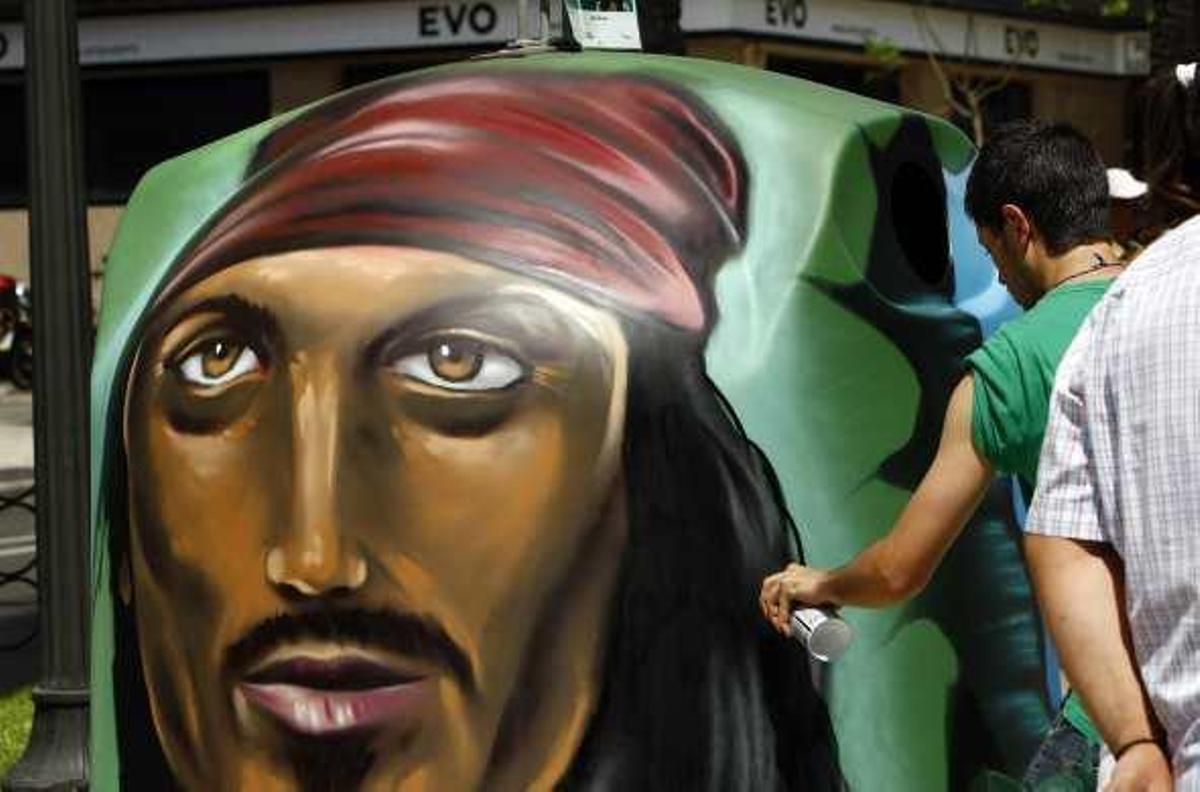 Un concursante da los últimos retoques a su grafiti en un contenedor de vidrio. A la derecha, el edil Llorens, en primer término, junto a la Bellea del Foc, observan a una dama infantil.