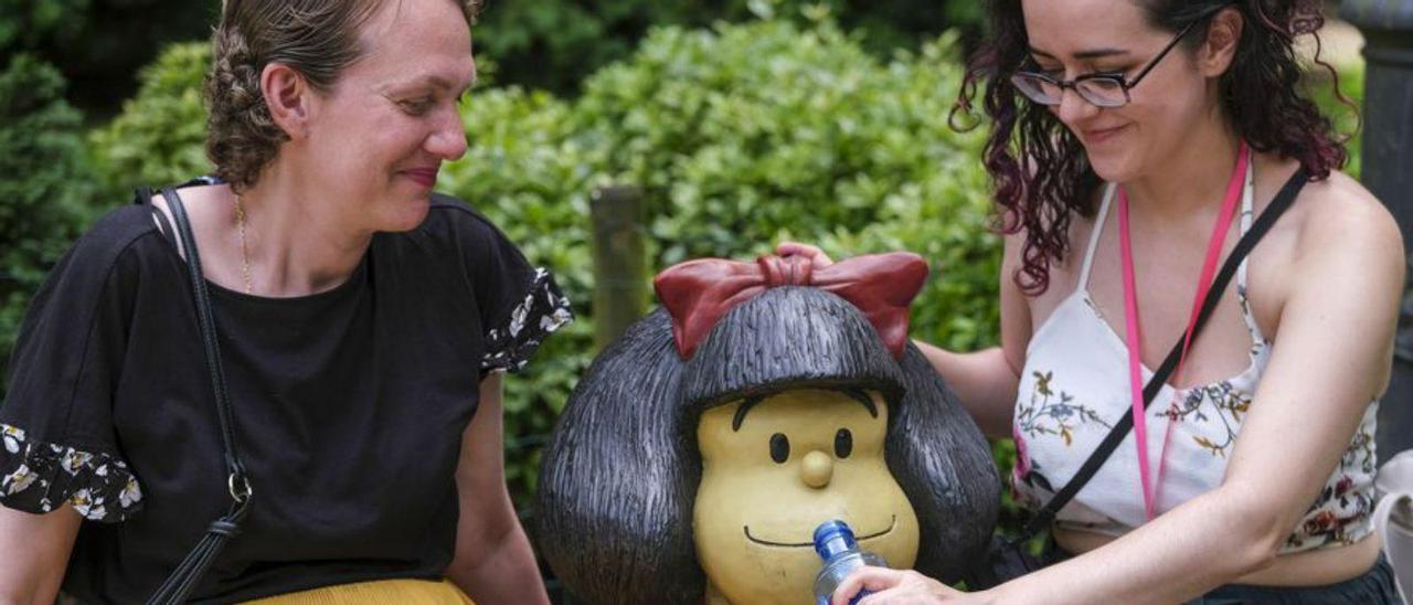 Dos mujeres dan de beber en broma a la estatua de Mafalda en el parque San Francisco de Oviedo. | Efe/ Paco Paredes