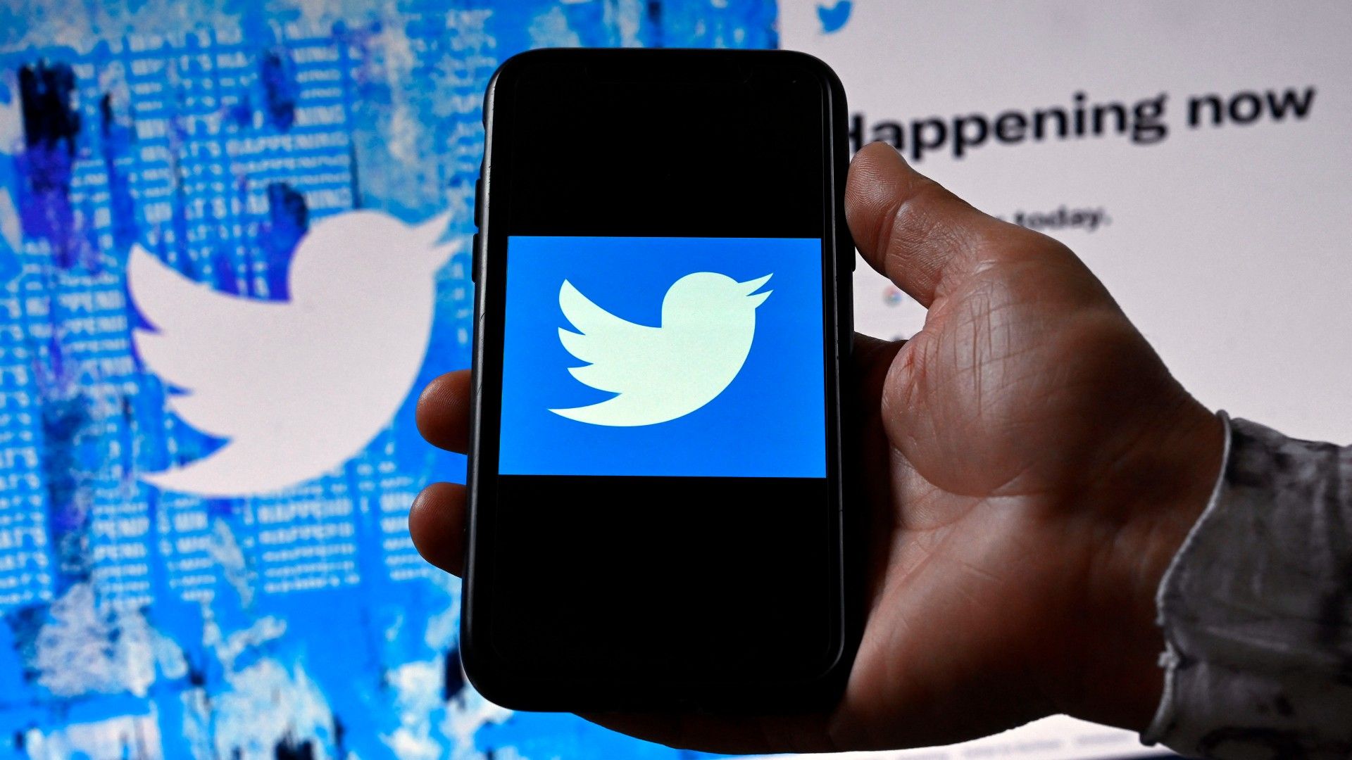 Una persona muestra el logo de Twitter en un móvil con un fondo que muestra, también, el logo de Twitter.