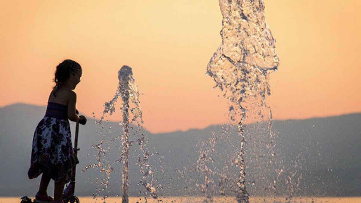 Una niña se refresca en una fuente.