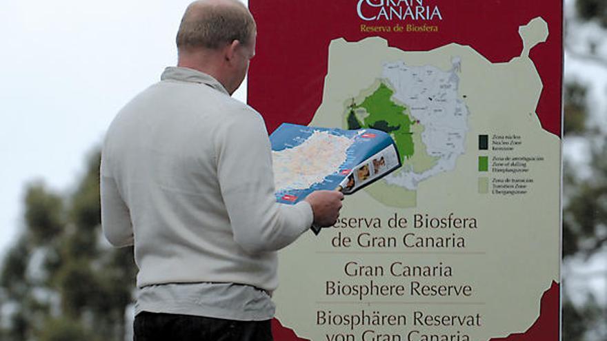 Un turista mira el mapa de la Isla frente a un cartel de la Reserva de la Biosfera en la GC-600.