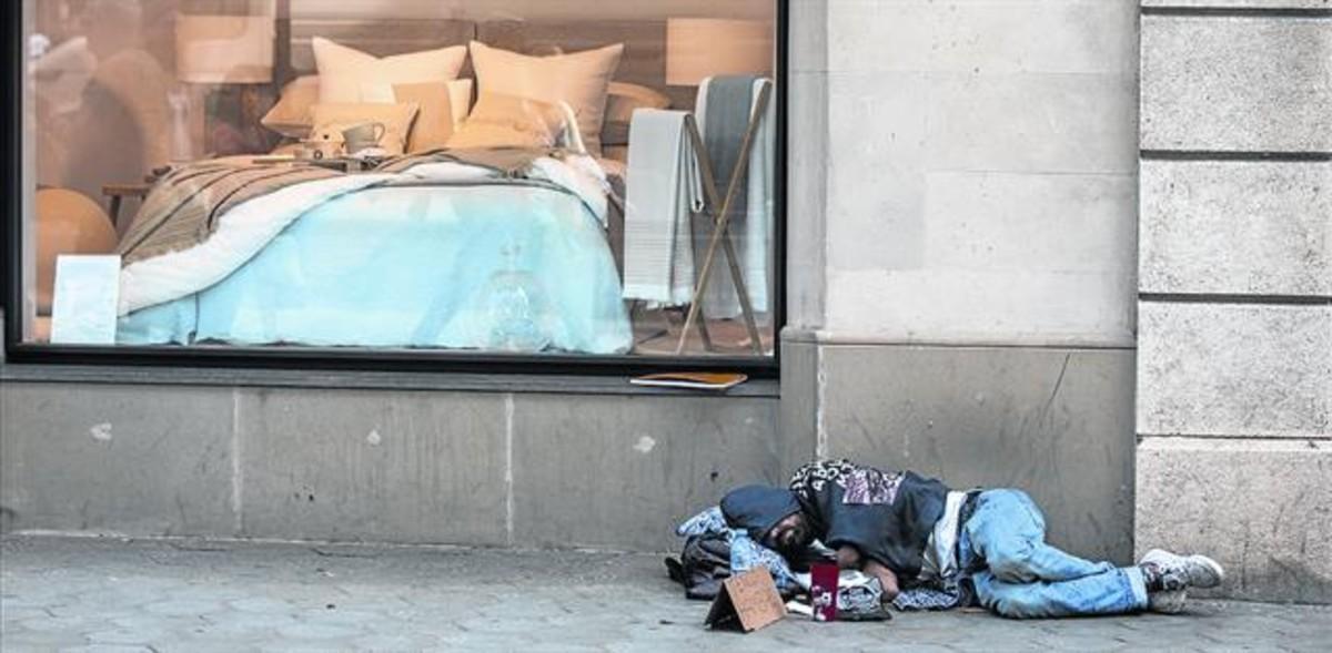 Un sintecho duerme junto al escaparate de una tienda de menaje, en el paseo de Gràcia, en una imagen de archivo.