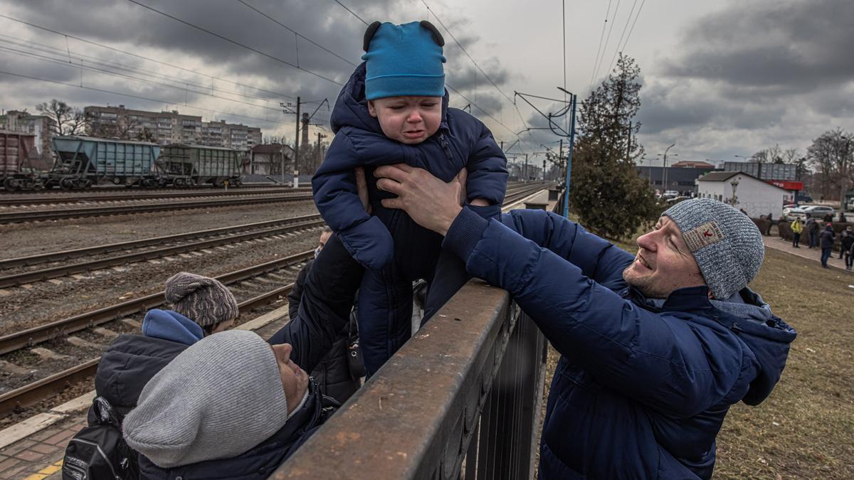 Oleg , que decidió permanecer en Irpin, pasa a su hijo Maksim por encima de una valla a su esposa Yana, antes de la llegada de un tren de evacuación a la ciudad de Kiev (Kiev), en la estación de tren de Irpin