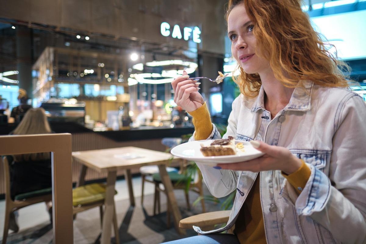 Una mujer come un trozo de tarta en una cafetería. Una mujer come un trozo de tarta en una cafetería.