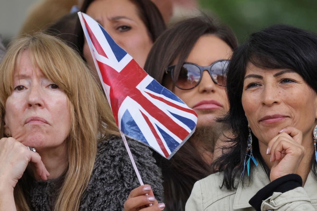 Ciudadanas con banderita esperan para dar el último adiós a Isabel II, en el recorrido de su féretro desde el palacio de Buckingham.