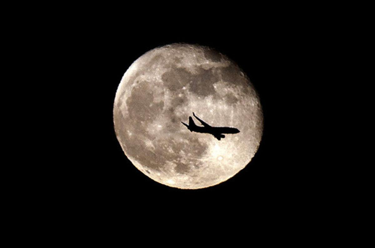 Un avió vola sobre Barcelona davant la Lluna que il·lumina la capital catalana.