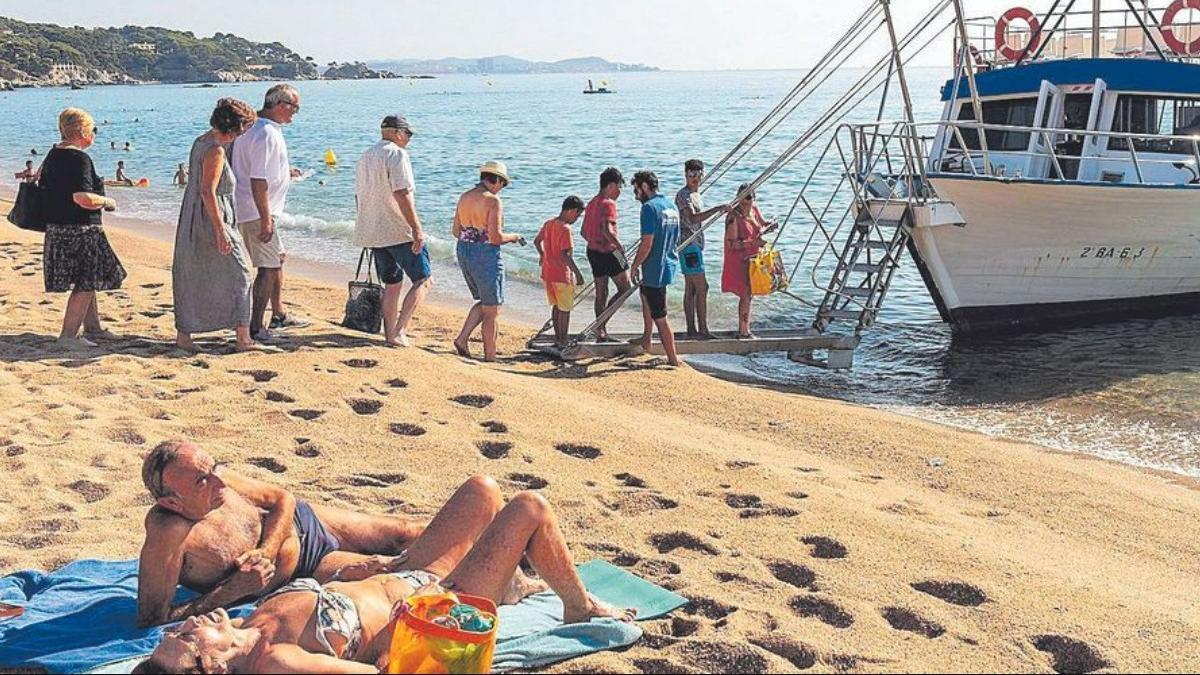 Un grupo de personas subiendo a una embarcación desde una playa de la Costa Brava