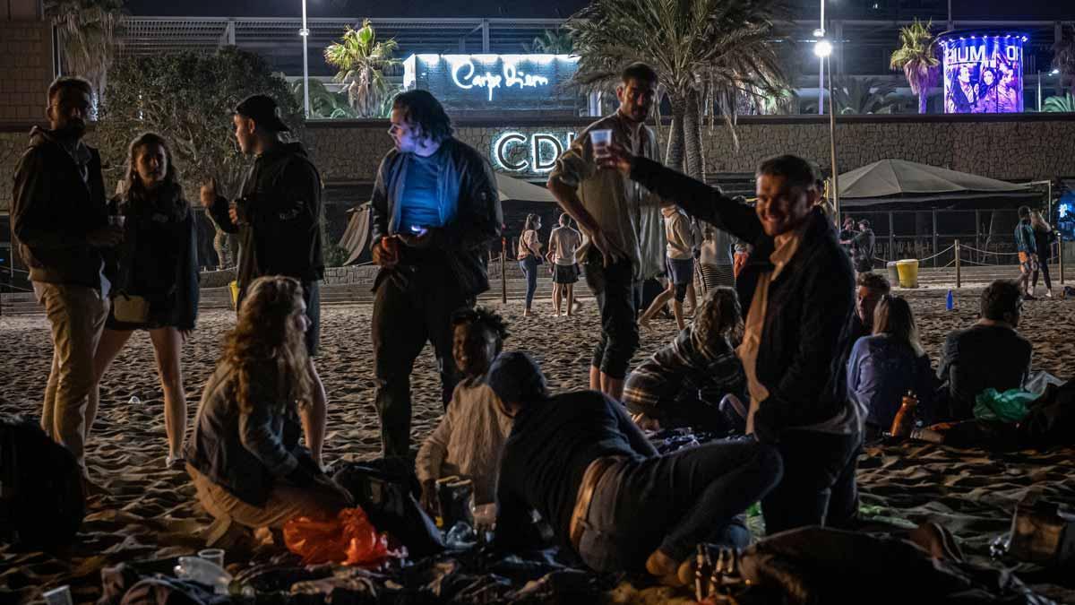 Unos jóvenes beben en la playa, frente a una zona de discotecas, en Barcelona